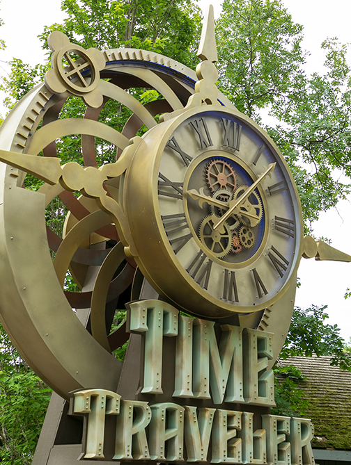 A large brass clock face and gear sculpture above lettering reading Time Traveler