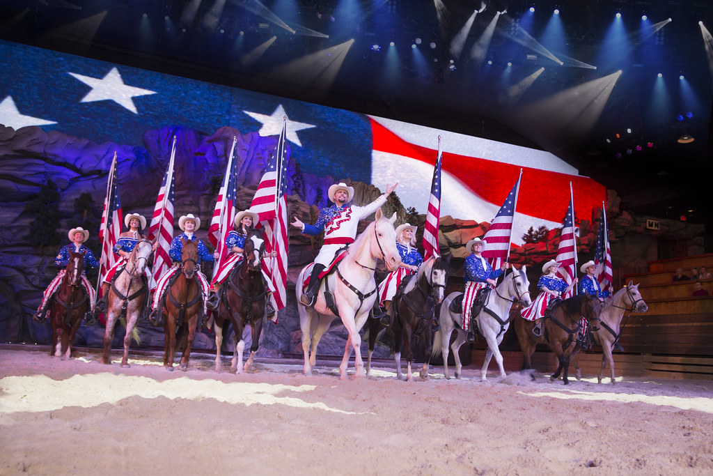 Riders carrying United States flags on horseback in the arena at Dolly Parton’s Stampede in Branson Missouri