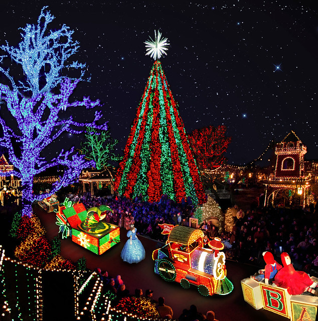 Towering Christmas tree lit in red and green beside a glowing train float and crowds at a night-time Branson Christmas lights display