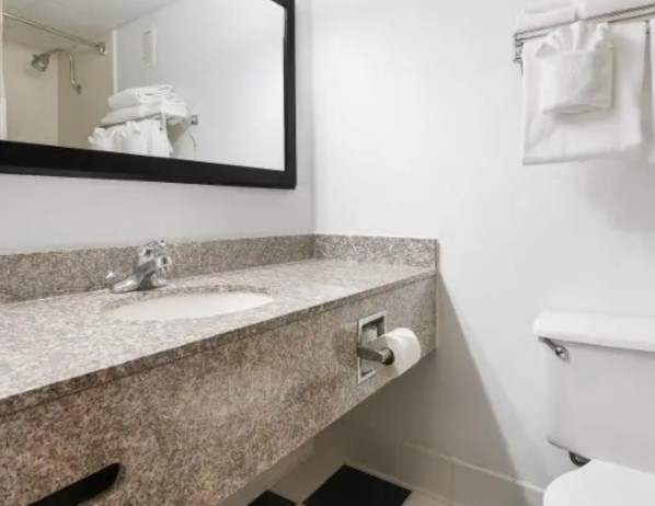A bathroom with a granite vanity, a framed mirror and a folded towel