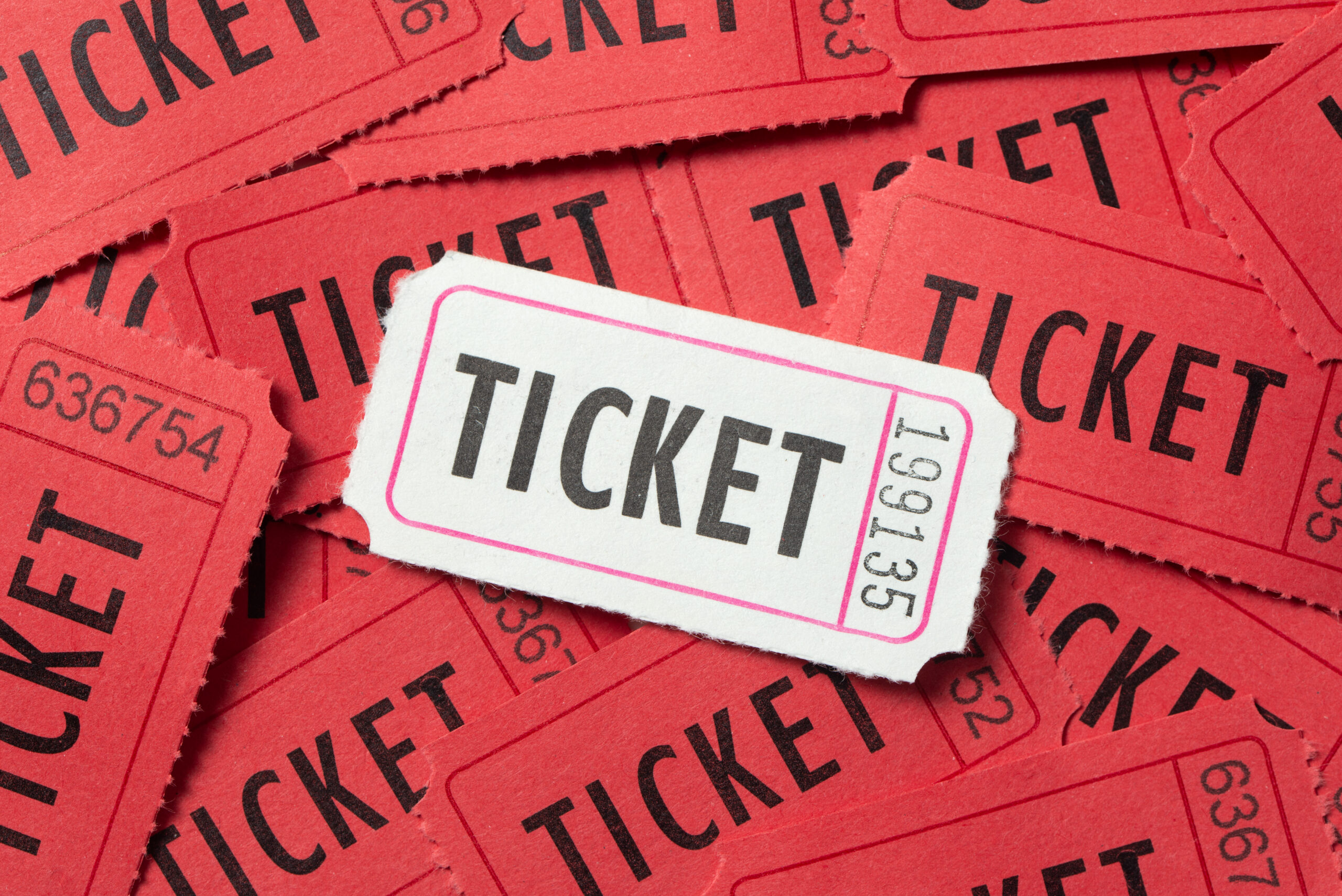 A single white admission ticket resting on top of a scattered pile of red paper tickets